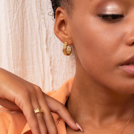 Geometric gold hoop earrings being worn with a gold ring