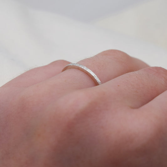 A close-up image of a silver textured ring on a person's finger.