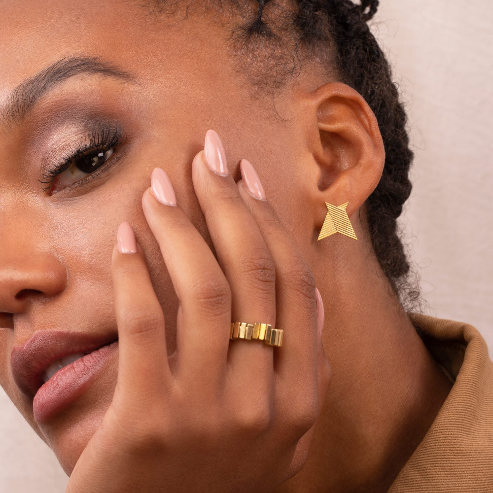 A person wearing a gold-coloured chevron earring with a geometric design.