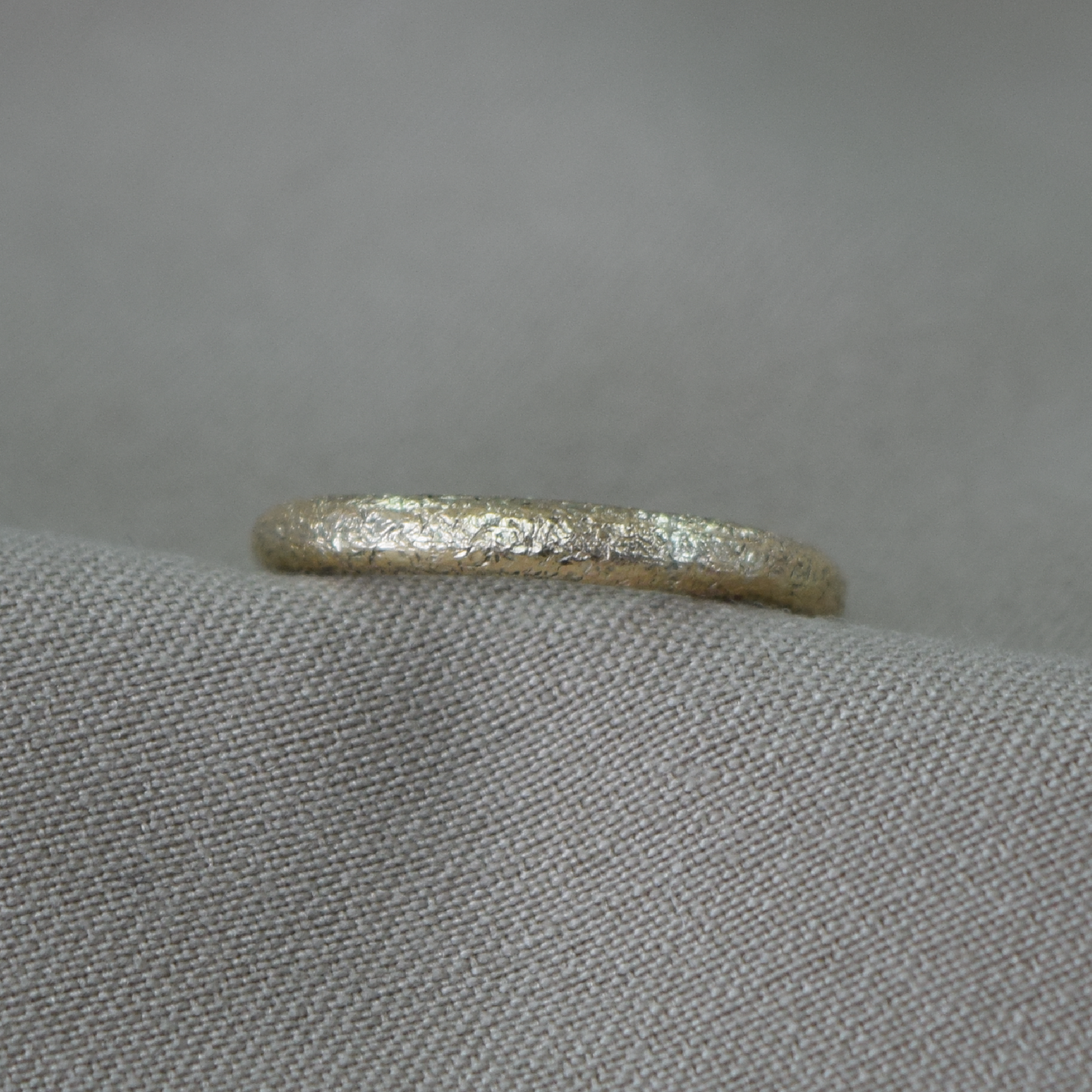 A textured gold band ring resting on a gray fabric surface.