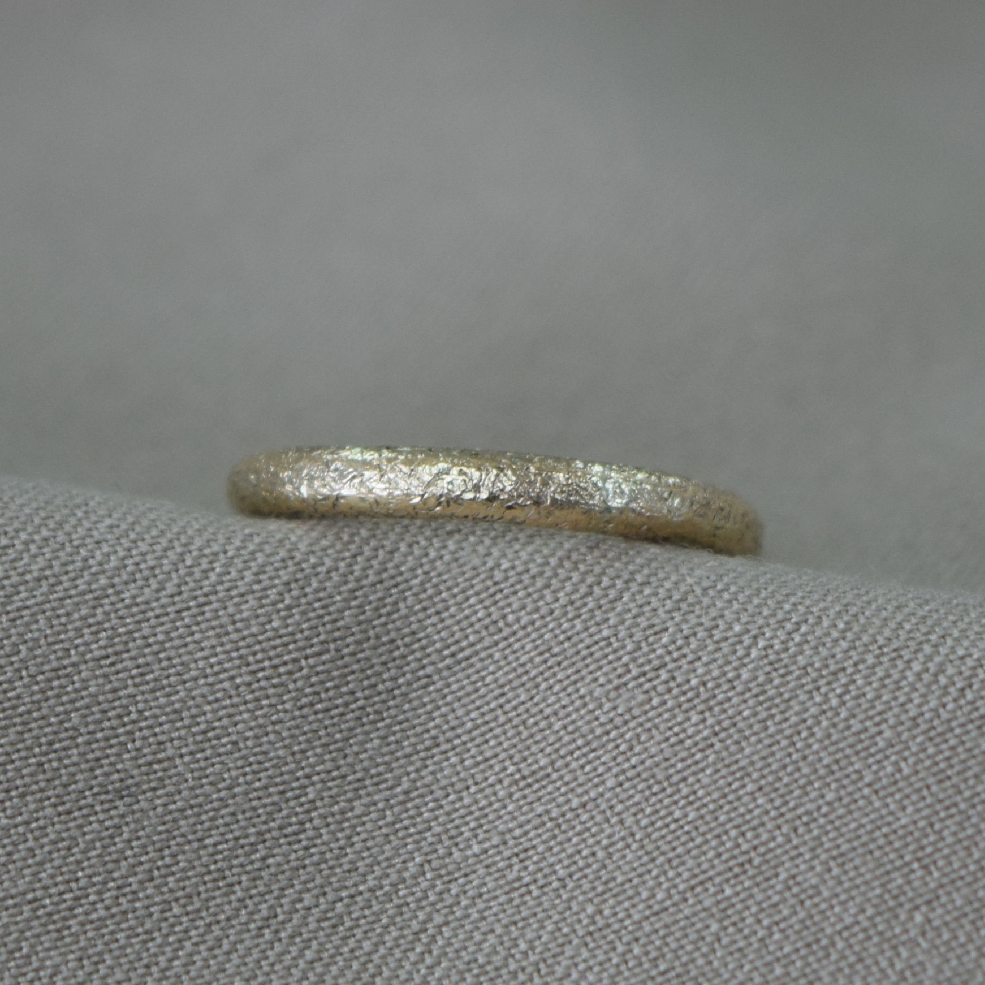 A textured gold band ring resting on a gray fabric surface.
