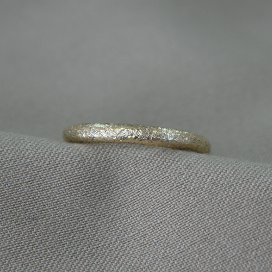 A textured gold band ring resting on a gray fabric surface.