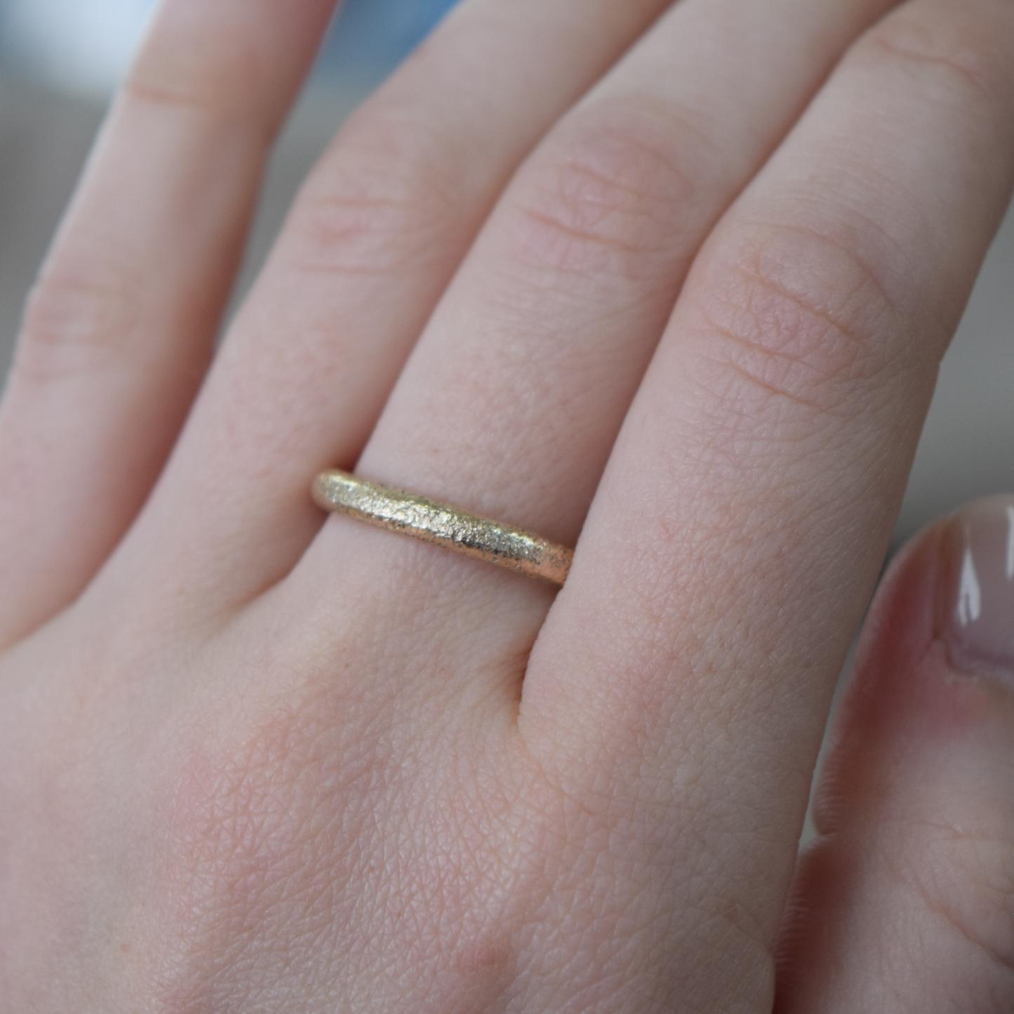 A close-up of a hand wearing a thin textured gold band ring.