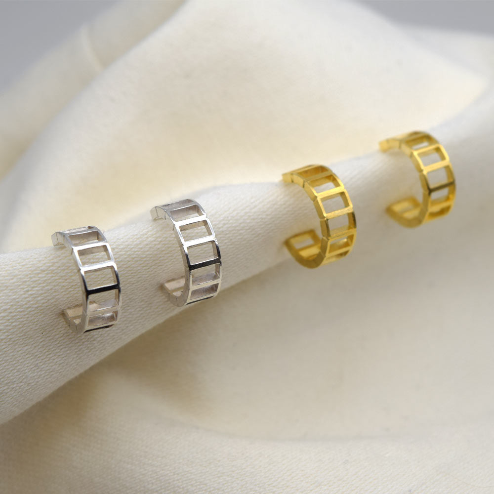 Silver and gold brick pattern hoop earrings on a beige fabric background