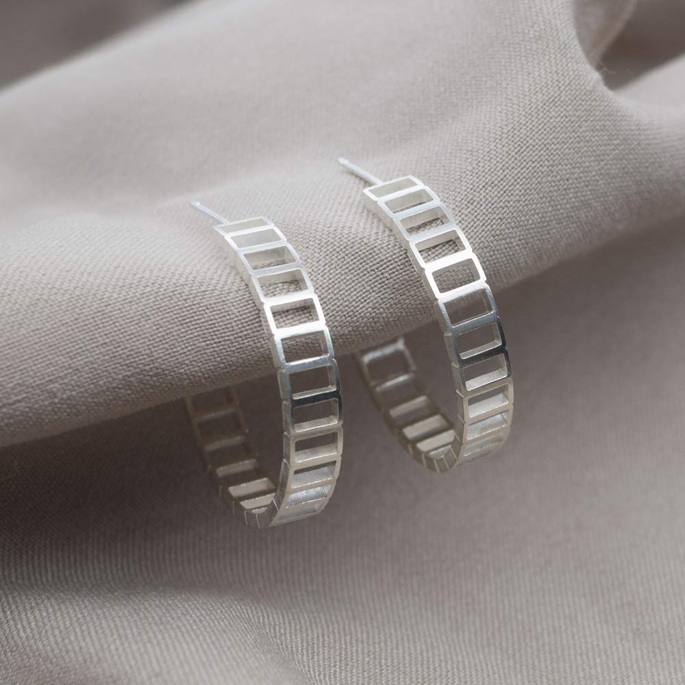 A pair of silver hoop earrings displayed on a beige fabric surface.