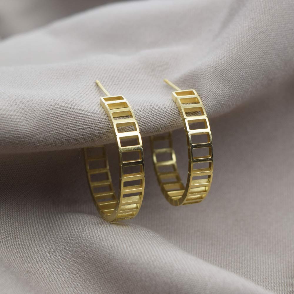 Large brickwork gold hoop earrings on a beige fabric background