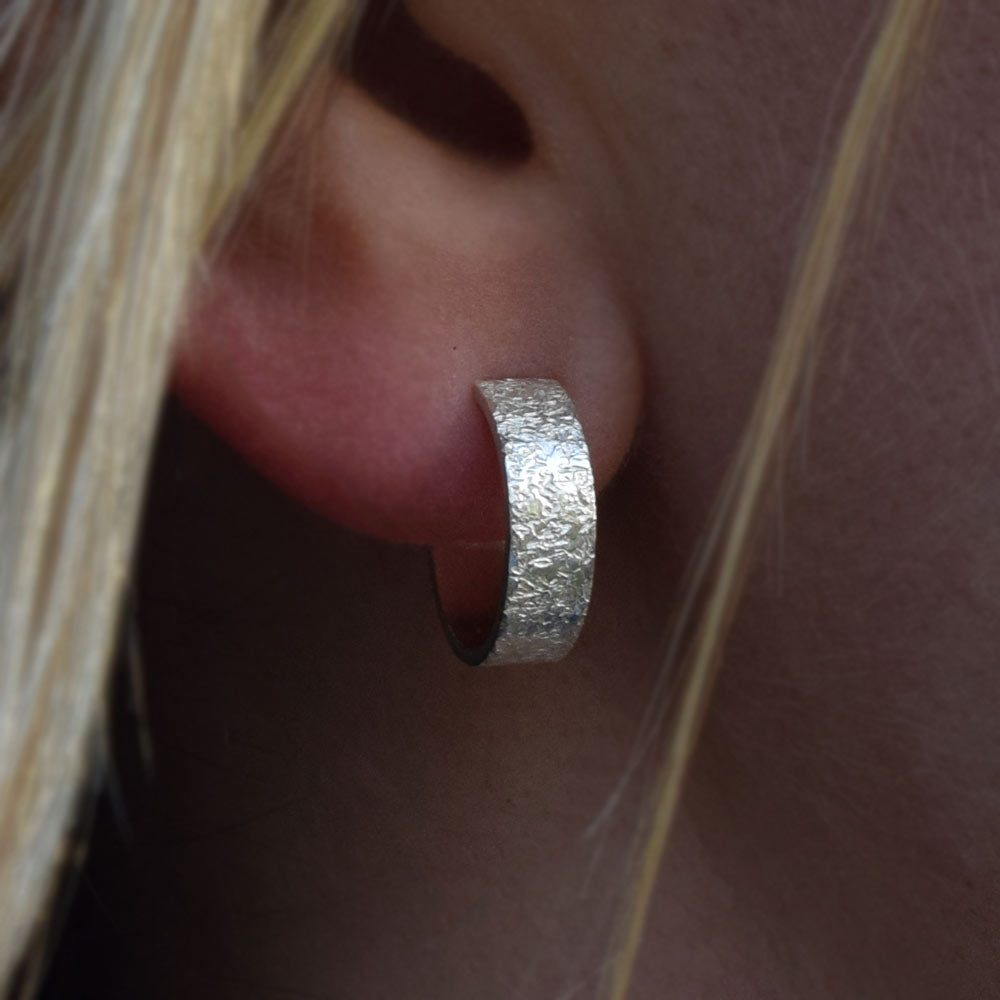 Small textured sterling silver hoops being worn on an ear