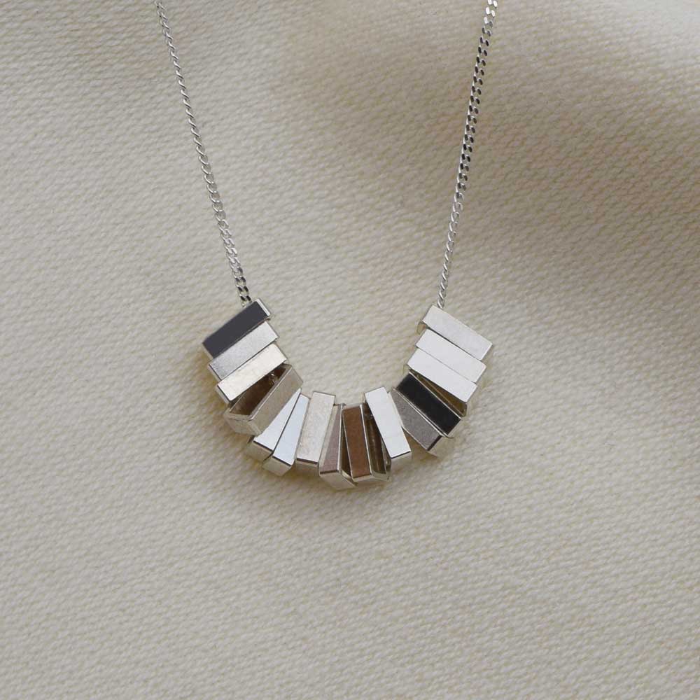 A silver geometric patterned necklace displayed against a neutral background.