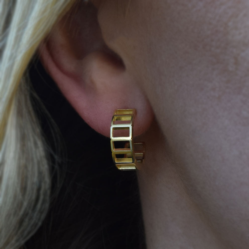 Gold geometric hoop earrings being worn on an ear