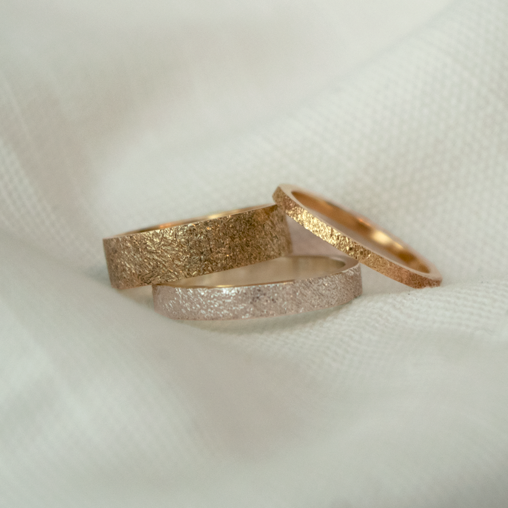 Three gold rings of different designs on a white fabric background