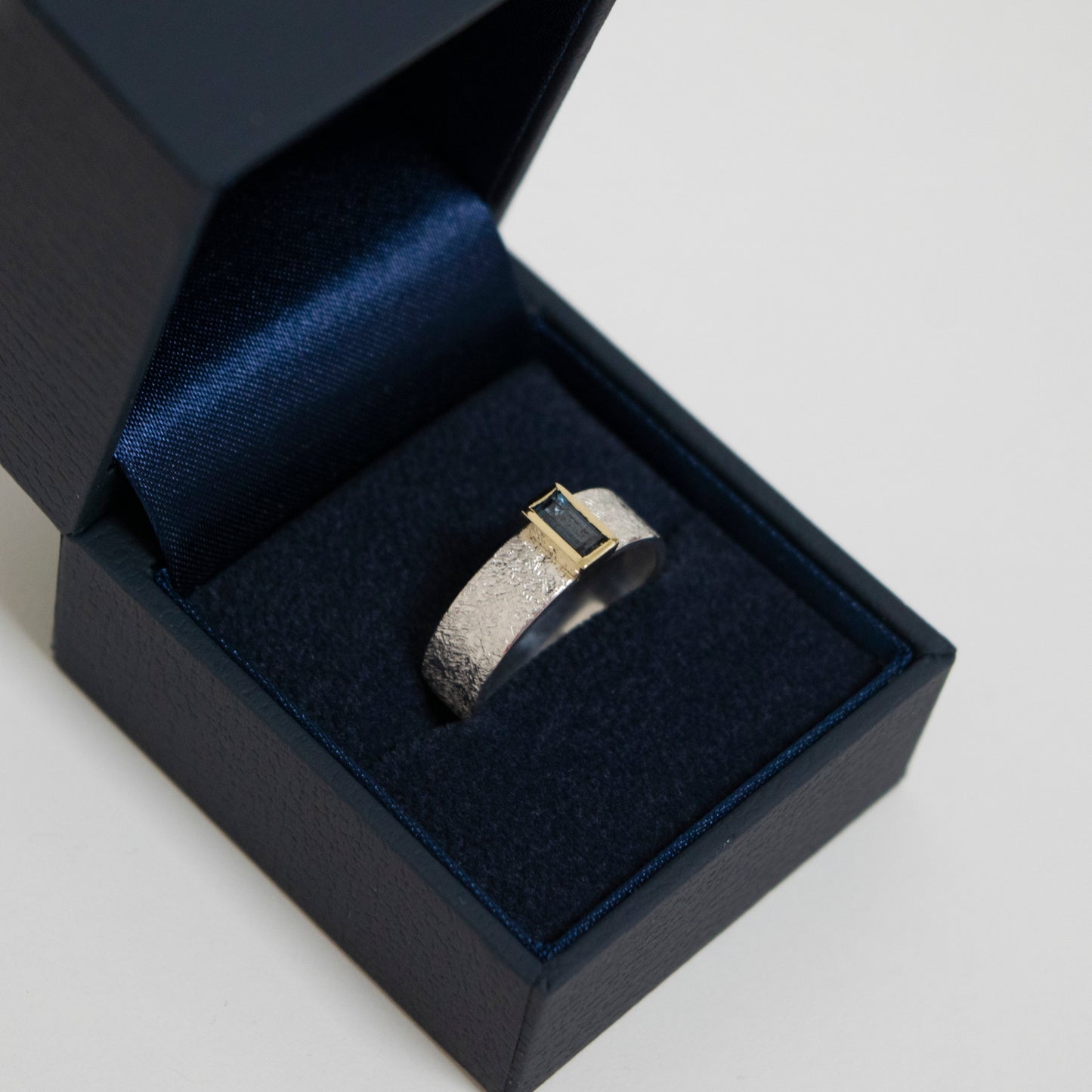 Silver ring with a black stone in a black jewelry box on a light gray background