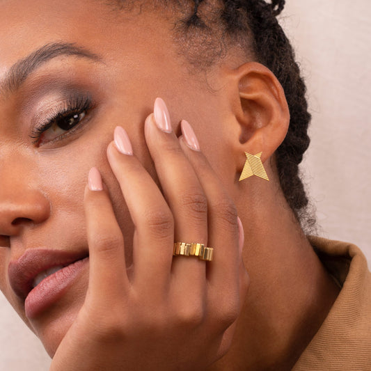 A person wearing a gold-coloured chevron earring with a geometric design.